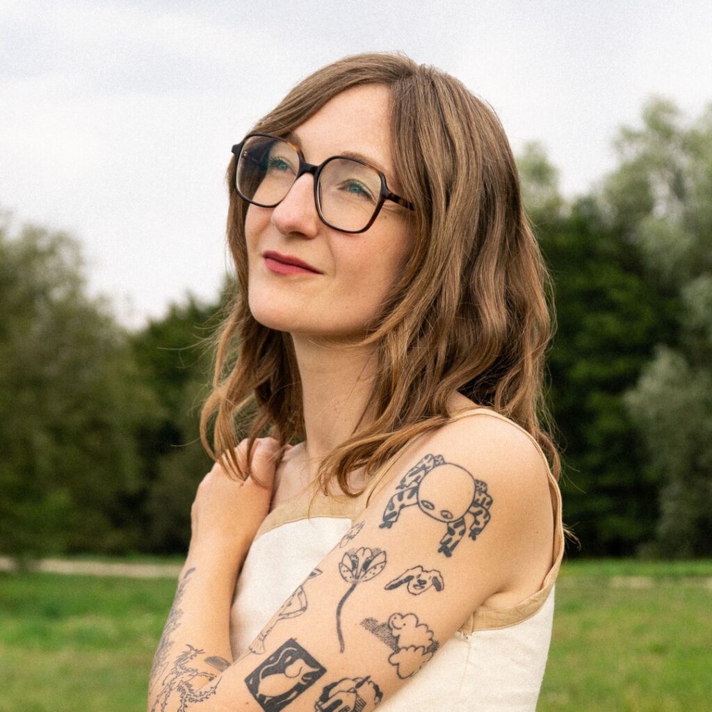 Ellie James en extérieur, lunettes noires et bras tatoués